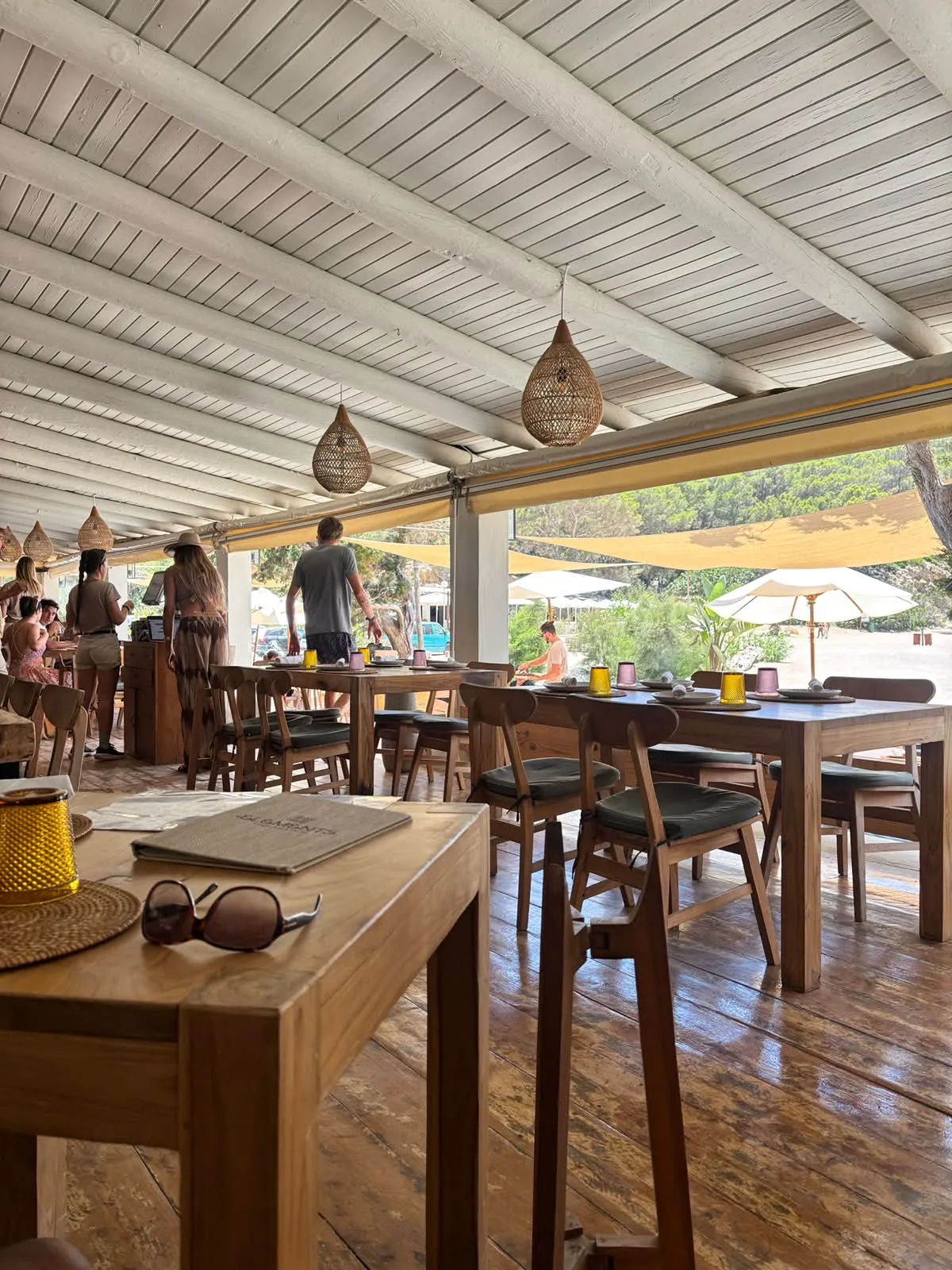 Lounge boho di Elements Ibiza con mobili in legno, bougainvillea e vele ombreggianti sopra Cala Benirràs