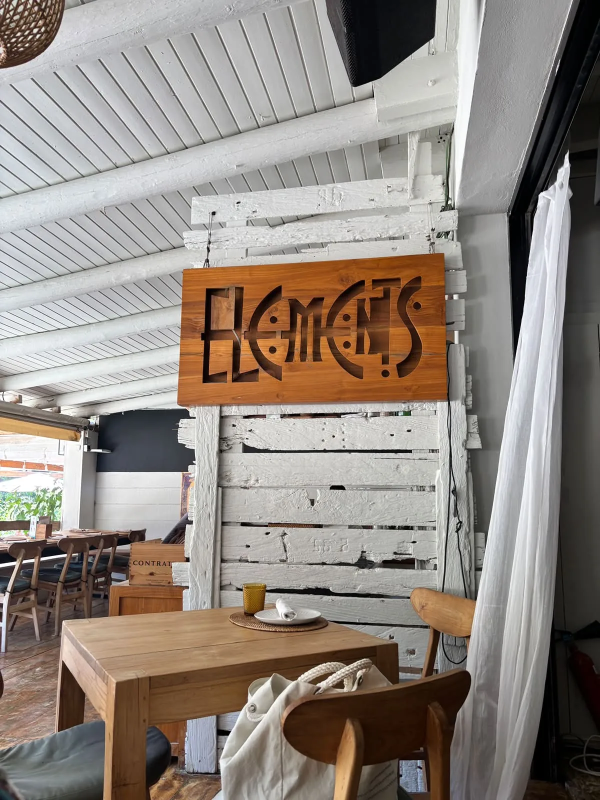 Insegna in legno con la scritta intagliata „Elements“ nel ristorante di Elements Ibiza sulla Cala Benirràs