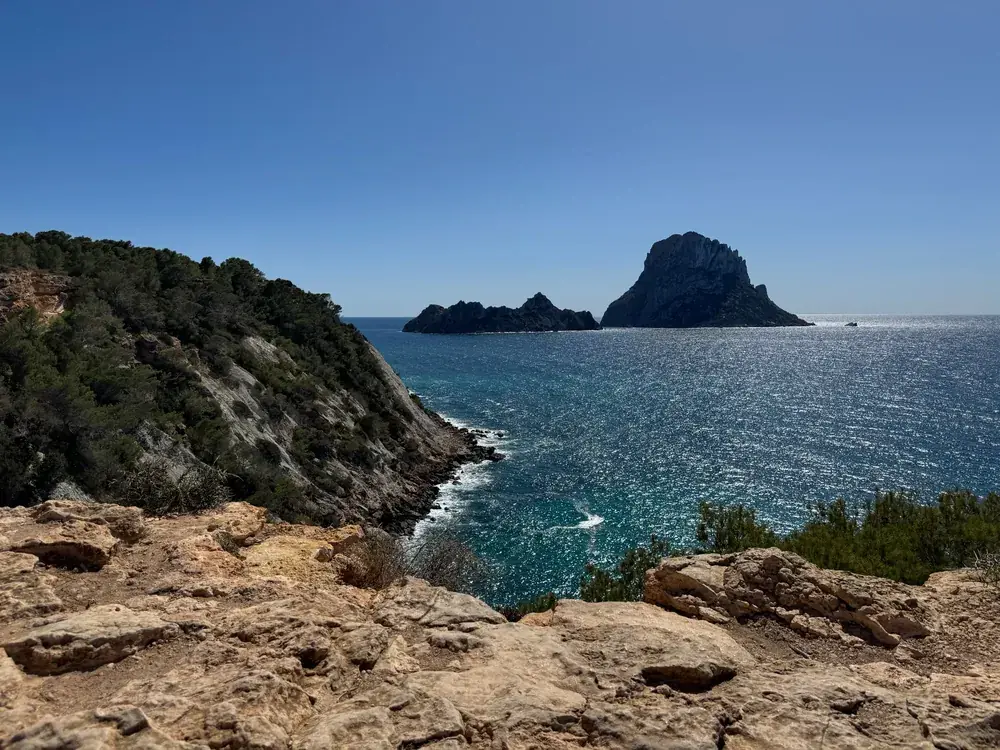 View over wooded cliffs and the shimmering sea to Es Vedrà and Es Vedranell