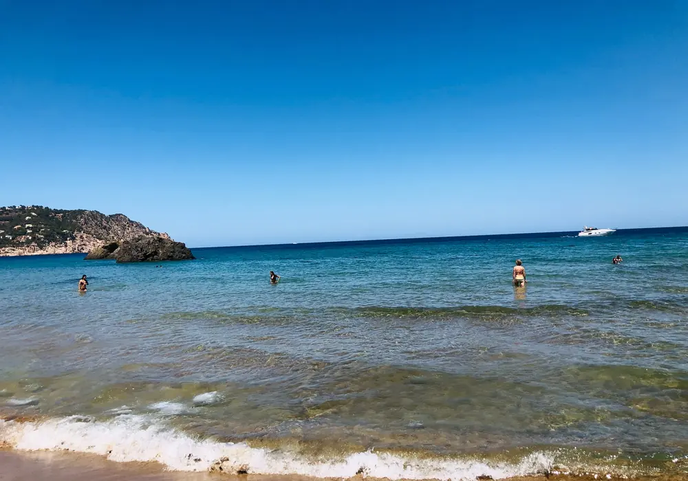 Klares blaues Wasser der Cala Boix mit Badenden und vorgelagertem Felsen