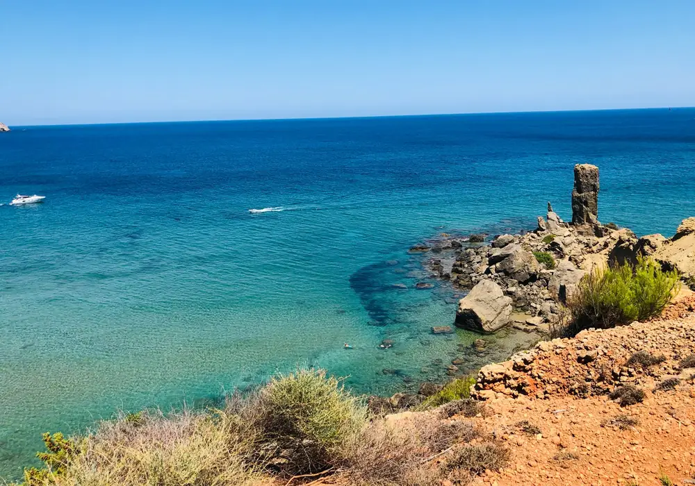 Blick von der roten Steilküste über das türkise Meer und die Felsnadel bei der Cala Boix