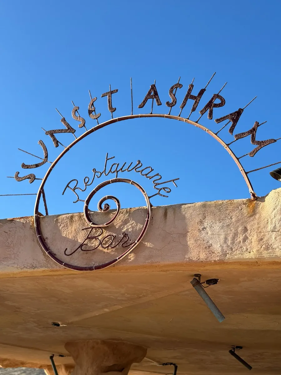 Geschwungenes Schmiedeeisen-Schild der Strandbar Sunset Ashram an der Cala Comte