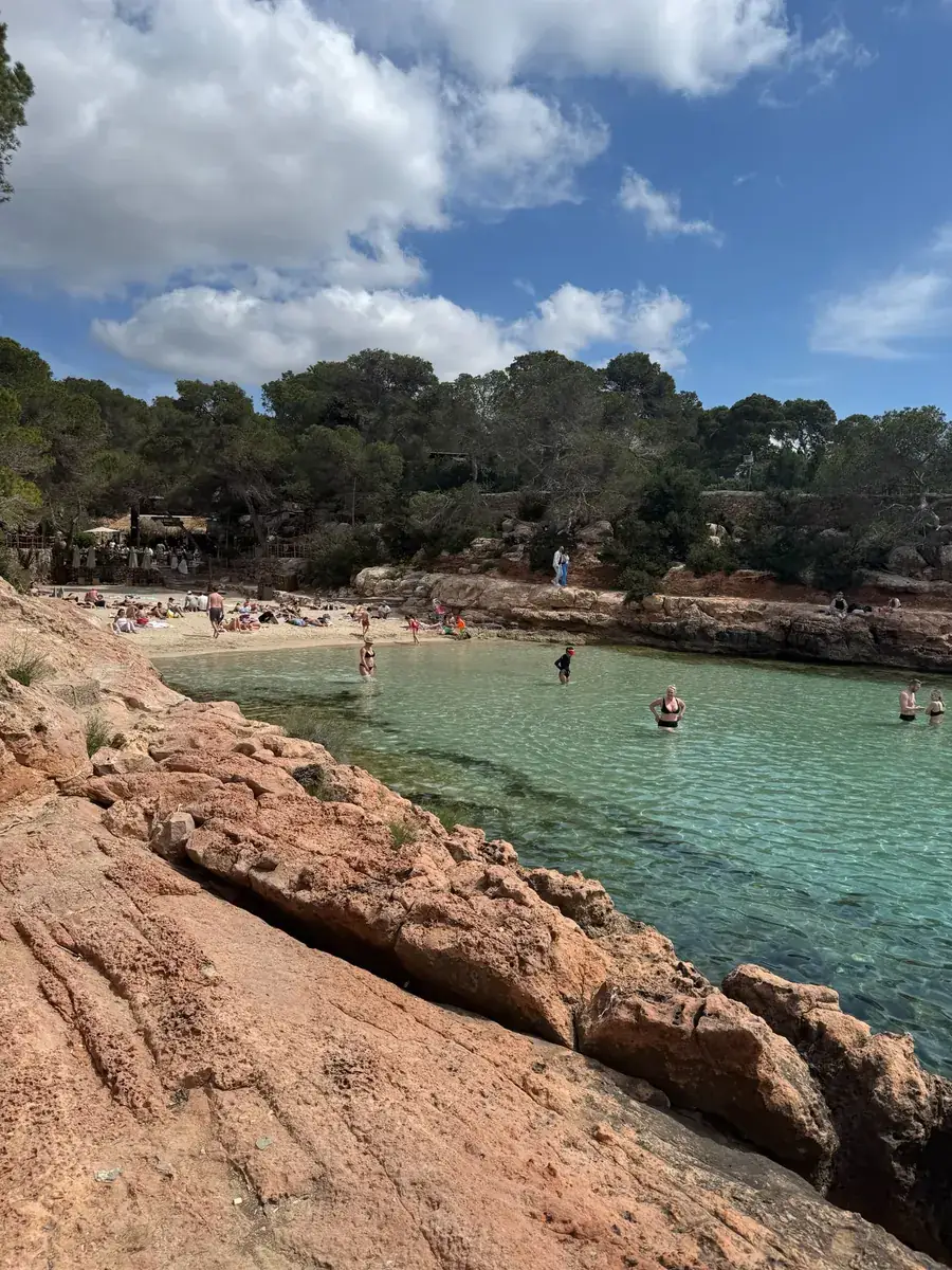 Glasklares türkises Wasser der Cala Gracioneta, umrahmt von rot-ockerfarbenen Felsen und Pinien
