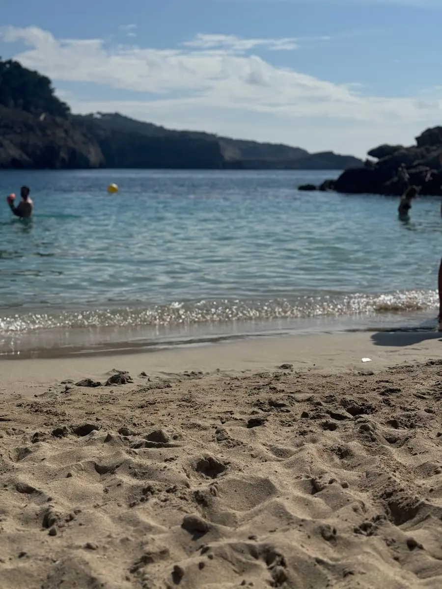 Sable clair et fin de Cala Saladeta avec une eau turquoise transparente et des pointes boisées