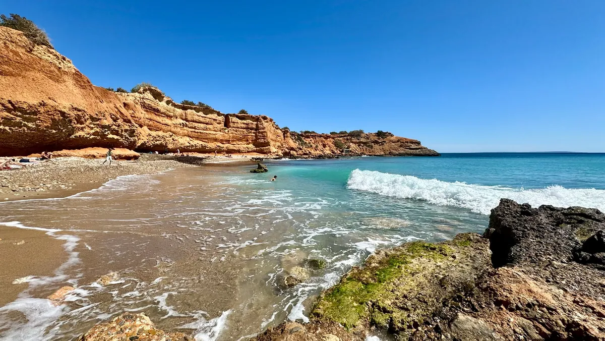 La houle sur Cala de Sa Caleta devant les falaises de grès brun rouge, avec des rochers au premier plan