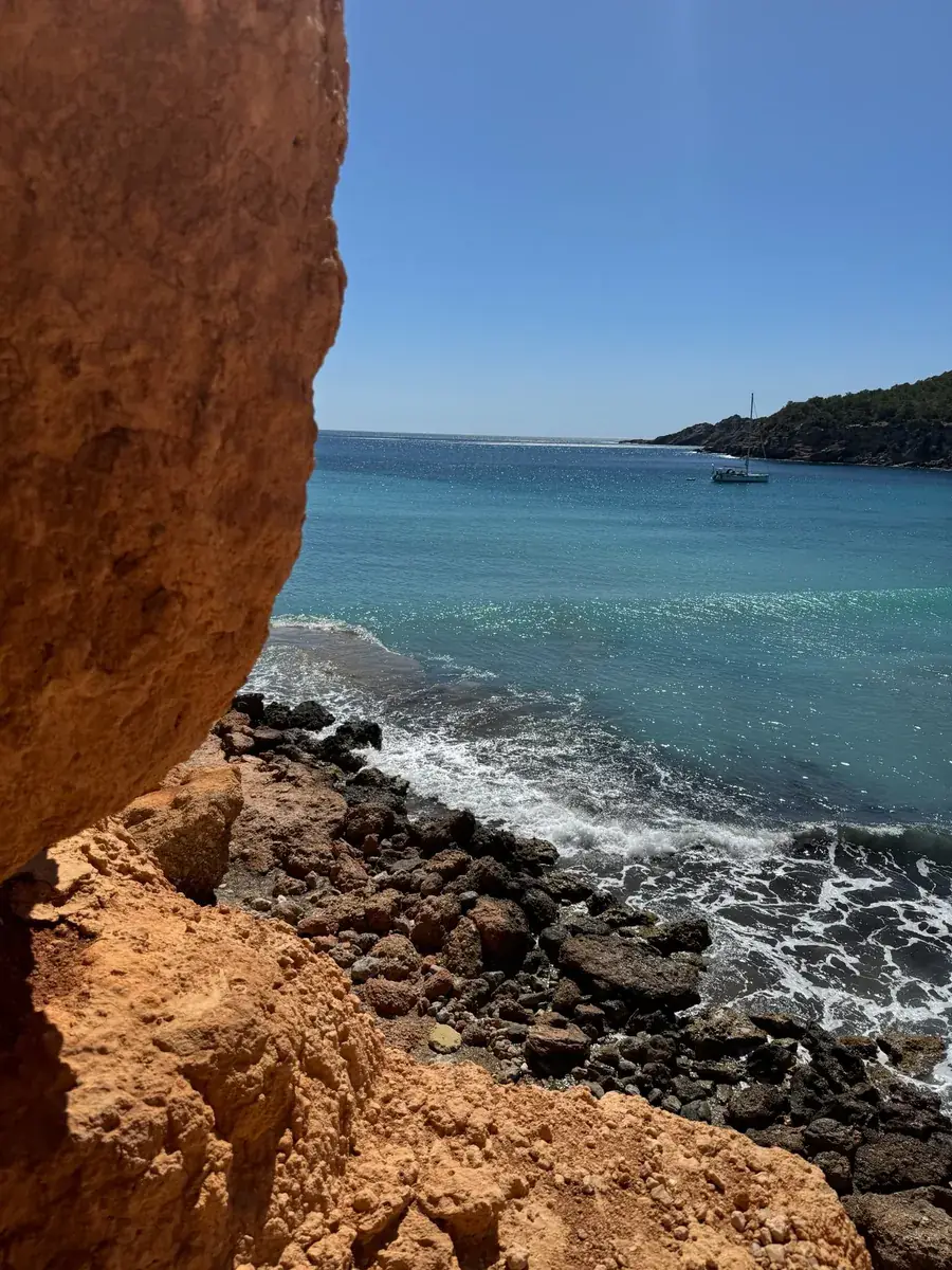 Vue depuis une grotte rocheuse près de Sa Caleta sur la côte rocheuse, la mer turquoise et un voilier au mouillage